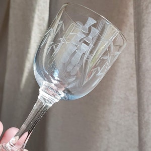 May include: A clear glass stemmed drinking glass with an etched design of bamboo stalks. The glass is held in a hand.