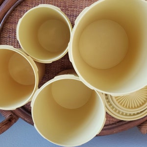 May include: Set of four yellow plastic containers with lids. The containers are nested inside each other, with the largest container at the bottom and the smallest container at the top.