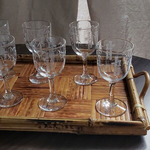 May include: A set of six clear glass wine glasses with etched designs sit on a brown bamboo tray with handles.