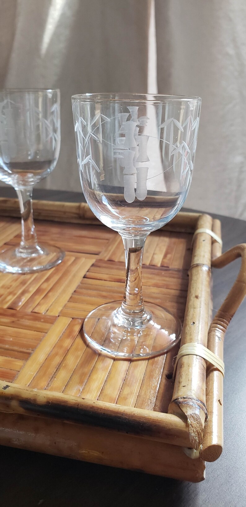 May include: Two clear glass shot glasses with etched bamboo designs on a bamboo tray. The glasses have a delicate stem and a round base.