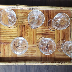 May include: A bamboo tray with six clear glass cups. The tray has a woven pattern and two handles.