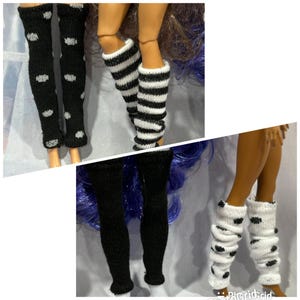 May include: A collection of miniature knit leg warmers for dolls, featuring various patterns including black with white polka dots, black and white horizontal stripes, solid black, and white with black polka dots, all designed for doll-sized legs.