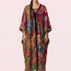 May include: A vibrant, patchwork-style caftan in shades of red, purple, blue, and green. The long, flowing garment features a lace-up neckline, red pom-poms, and gold trim. The sleeves are wide, and the caftan is worn with black boots.
