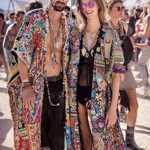 May include: Two people wearing colorful, patterned kimonos and sunglasses. The kimonos feature a vibrant mix of colors and intricate designs. The man wears a beaded necklace and a decorated hat. The woman wears a black top and a backpack.