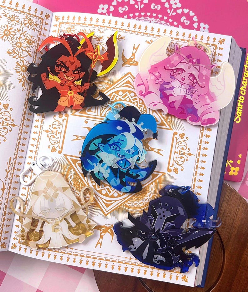 Op de afbeelding: Vijf acryl bedels met diverse ontwerpen: een rode demon met een wapen, een roze gevleugelde figuur, een blauw personage in narrenstijl, een wit geklede figuur met gouden accenten en een donkerblauwe gepantserde ridder met een zwaard.