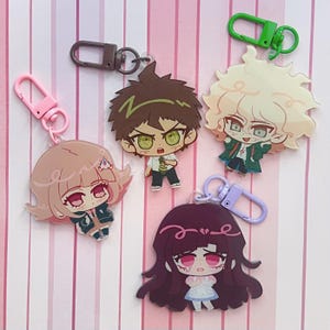 Peut inclure: Quatre porte-clés en acrylique représentant des personnages de style anime avec des cheveux et des tenues distincts. Chaque breloque comprend un fermoir mousqueton en plastique rose, marron, vert ou violet clair sur une base en acrylique.