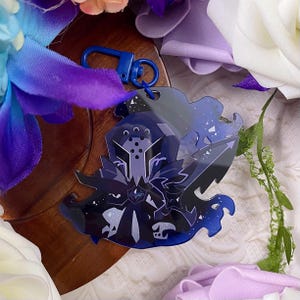 Op de afbeelding: Een donkerblauwe acryl sleutelhanger met een gestileerde karakterillustratie voorzien van een helm, scherpe geometrische bepantsering en vloeiende cape-elementen. Het ontwerp bevat marineblauwe en violette gradi&euml;nten met witte sterachtige accenten.
