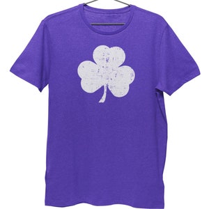 Pode incluir: Uma camiseta roxa com um gr&aacute;fico de trevo branco desbotado.
