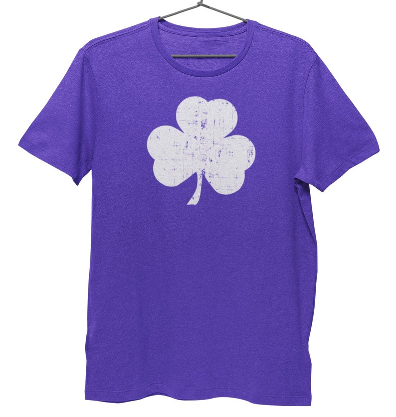 Pode incluir: Uma camiseta roxa com um gr&aacute;fico de trevo branco desbotado.