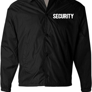 Op de afbeelding: Zwarte beveiligingsjas met het woord "SECURITY" in witte blokletters. De jas heeft een knoopsluiting aan de voorkant, een kraag en elastische manchetten. Het NYC Factory-logo is zichtbaar op het label.