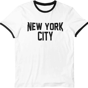 May include: White t-shirt with a black ringer neck and the text "NEW YORK CITY" printed in black.