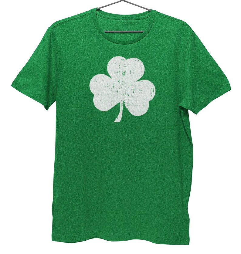 Pode incluir: Uma camiseta verde com um design de trevo branco desbotado.