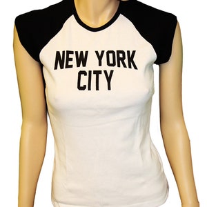May include: White t-shirt with black raglan sleeves and the text "NEW YORK CITY" printed in black.