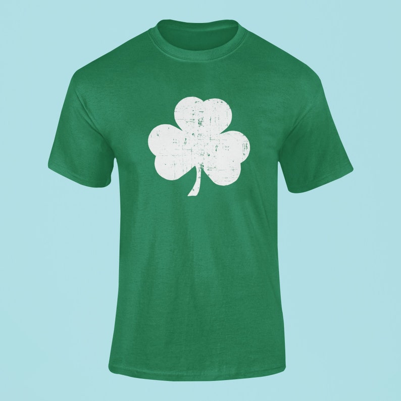 Pode incluir: Uma camiseta verde com um design de trevo branco desbotado.