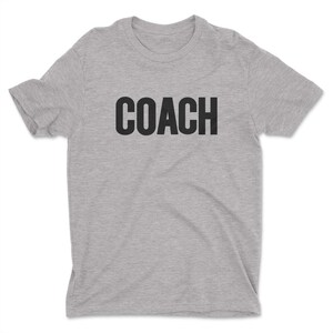 K&ouml;nnte beinhalten: Ein hellgraues T-Shirt mit dem Wort "COACH" in Schwarz gedruckt.