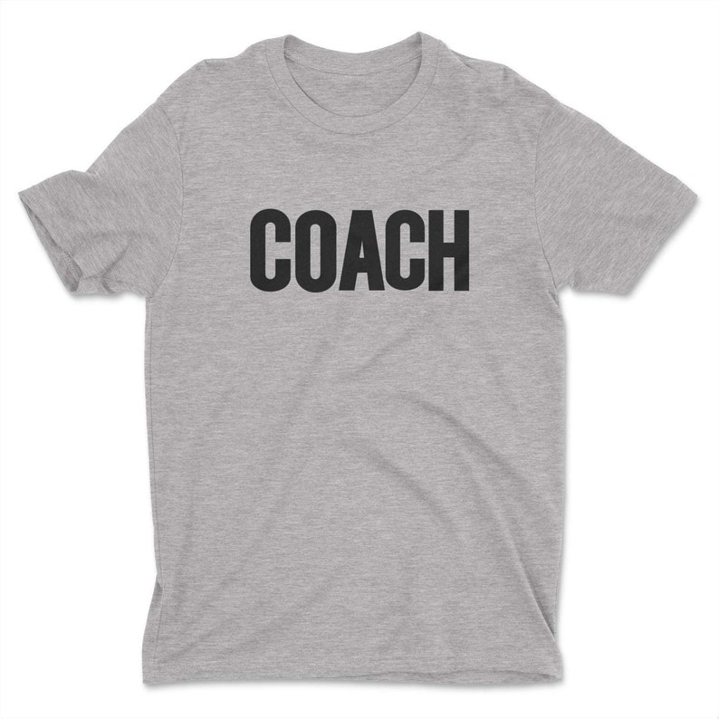 K&ouml;nnte beinhalten: Ein hellgraues T-Shirt mit dem Wort "COACH" in Schwarz gedruckt.