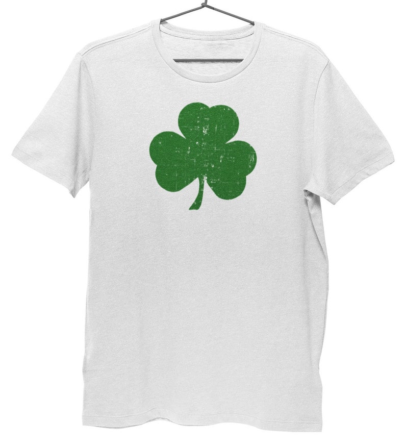 Pode incluir: Camiseta branca com um gr&aacute;fico de trevo verde. O trevo tem um visual desgastado e vintage.
