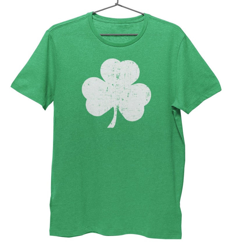 Pode incluir: Uma camiseta verde com um design de trevo branco desbotado.