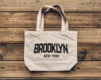 May include: A white canvas tote bag with black handles and the text "BROOKLYN NEW YORK" printed on the front.