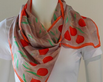 May include: A silk scarf with a gray background, featuring a pattern of red and green floral designs. The scarf has an orange border and is draped around a mannequin's neck.