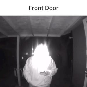 以下が含まれることがあります： 防犯カメラからの白黒画像。白いフード付きスウェットを着た人物がドアの前に立っています。「blink」の文字が左上に表示されています。「Front Door」の文字が上部に表示されています。