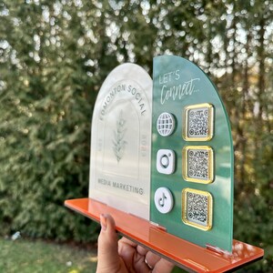 Peut inclure: Une r&eacute;compense en acrylique blanche et verte avec le texte "Edmonton Social Media Marketing" et un motif de plante. La r&eacute;compense comporte une section verte avec le texte "Let's Connect..." et trois codes QR avec des ic&ocirc;nes pour Instagram, TikTok et un globe.