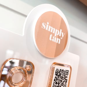 May include: A white and rose gold round sticker with the text "simply tan" in white. A rose gold Instagram icon and a rose gold QR code are also visible.