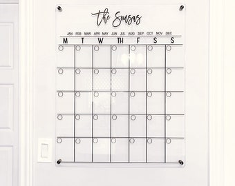 May include: A clear acrylic dry erase calendar with the text "The Sousas" at the top. The calendar has the months of the year listed across the top and the days of the week listed below. There are circles for each day of the month.