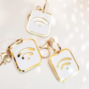Può includere: Tre portachiavi dorati con ciondoli quadrati bianchi che presentano un simbolo wifi dorato.
