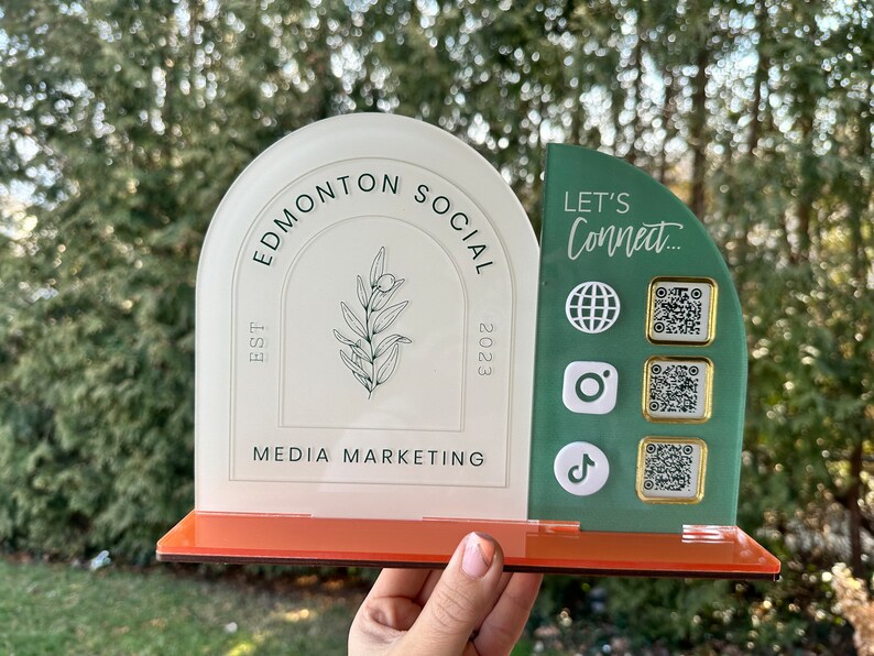 Peut inclure: Panneau en acrylique blanc et vert avec le texte "Edmonton Social" et "EST 2023" et "Media Marketing". Le panneau comporte &eacute;galement un petit motif de branche d'olivier. Sur le c&ocirc;t&eacute; droit du panneau se trouve un panneau en acrylique vert avec le texte "Let's Connect..." et quatre carr&eacute;s blancs avec des ic&ocirc;nes et des codes QR.