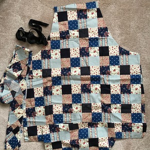 Peut inclure: Un tablier en patchwork avec un motif floral bleu, blanc et rouge. Le tablier a une grande poche et deux liens.