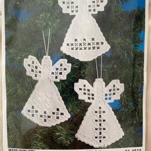 May include: Three white embroidered angel ornaments with intricate cutwork patterns, each featuring a hanging loop. The packaging displays the brand name Permin, the text Scandinavian art needlework, and dimensions of 10 x 15 cm or 4 x 6 inches.