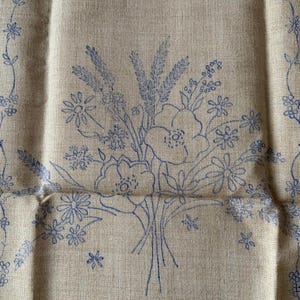 May include: A tan fabric featuring a blue line art print of a wildflower bouquet. The design includes various flowers, wheat stalks, and small blossoms. The fabric has a visible woven texture, and the blue ink outlines the botanical elements clearly.