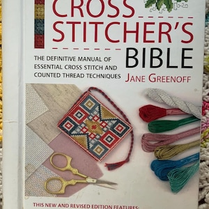 May include: The New Cross Stitcher's Bible book cover. The book features the title in large red letters, with the author's name, Jane Greenoff, below. The cover also displays cross-stitch examples, embroidery floss, and gold scissors.