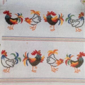 May include: A white fabric featuring a cross-stitch pattern of eight roosters arranged in two horizontal rows. The roosters alternate between white and dark-coloured bodies with red combs and multi-coloured tail feathers. Horizontal stripes border the rows.