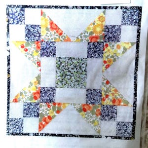 May include: A patchwork quilt block with a star pattern. The design incorporates a central square of small green floral fabric, surrounded by white, floral triangles, and blue and yellow floral squares. The border is a dark blue and white pattern.