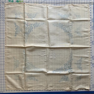 Stamped linen tablecloth with floral Daisy design in each of the four corners. It measures approximately 32” square.