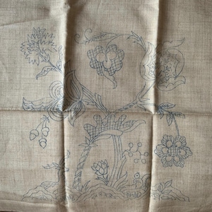 May include: A light tan linen fabric featuring a dark blue ink outline of a botanical design. The pattern includes various flowers, leaves, berries, a small deer, and a squirrel, all rendered in a simple, clean line art style for embroidery.