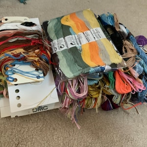 Könnte beinhalten: Eine Sammlung von Stickgarn in verschiedenen Farben, darunter Grün, Orange, Gelb, Blau, Rosa und Braun. Die Fäden sind auf weißen Pappkarten mit dem DMC-Logo organisiert und befinden sich in einer durchsichtigen Kunststoffverpackung mit der Aufschrift 8m.