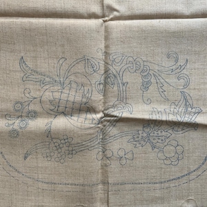 Könnte beinhalten: Ein beigefarbener Leinenstoff mit einem blauen Stickmuster aus einem floralen Muster. Das Design umfasst Blätter, Blumen und Spiralen.