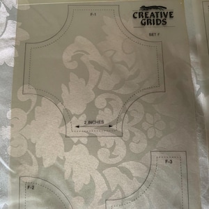 以下が含まれることがあります： Creative Grids Set Fとラベル付けされた透明なプラスチック製のキルティングテンプレートシート。シートにはF-1、F-2、F-3とマークされた3つの異なる形状があり、2インチと3インチの測定値が印刷されています。テンプレートには黒い輪郭とテキストが含まれています。