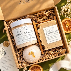 May include: A gift box containing a 9 oz jar of Walnut Body Scrub, a 4.5 oz bar of Indian Bay Black Walnut Soap on a wooden dish, and a round bath bomb. The box includes a card with the Hera by Hera logo and text about self-care rituals.