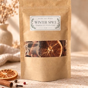 May include: A brown kraft paper pouch containing Winter Spice simmer pot potpourri. The label reads HERA BY HERA, WINTER SPICE, SIMMER POT POTPOURRI, 85g. A clear window reveals dried orange slices and spices inside the sealed stand-up bag.
