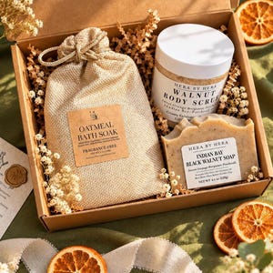 May include: A cardboard gift box containing a beige burlap drawstring bag labeled Oatmeal Bath Soak, a white jar of Walnut Body Scrub, and a rectangular bar of Indian Bay Black Walnut Soap, all nestled in brown paper filler with dried flowers.