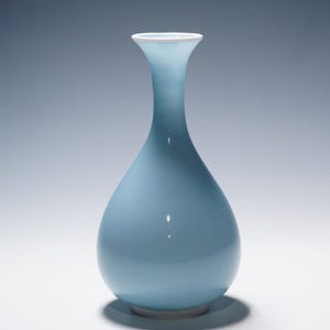 May include: A light blue, teardrop-shaped vase with a white rim. The vase has a smooth, glossy finish and a classic, elegant design. The vase is approximately 10 inches tall.