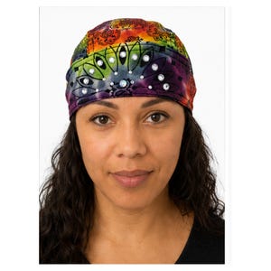 May include: A tie-dye skull cap featuring a vibrant rainbow color palette of red, orange, yellow, green, blue, and purple. The fabric is decorated with a black paisley-inspired pattern and embedded with clear, circular rhinestones in a fan shape.