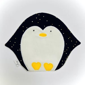 May include: A navy blue penguin-shaped baby bib with gold glitter accents. The bib features a white belly, yellow feet, and a yellow beak. The brand name "CAMILE&CO" is printed on a small white tag.