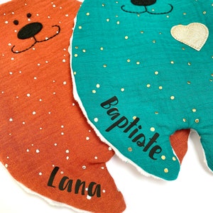 May include: Two plush bear-shaped baby blankets with embroidered faces. The blanket on the left is orange with white polka dots and the name "Lana" embroidered on it. The blanket on the right is teal with gold polka dots and the name "Baptiste" embroidered on it.