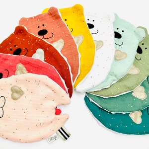 May include: A set of ten colourful, soft, plush bear-shaped baby toys with embroidered faces and gold hearts. The toys are arranged in a rainbow pattern.