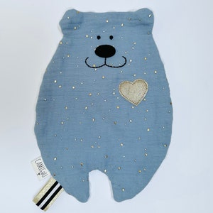 May include: A light blue plush bear with a gold heart and gold glitter. The bear has a black embroidered nose and mouth. The bear has a white tag that says "Camille" on it.